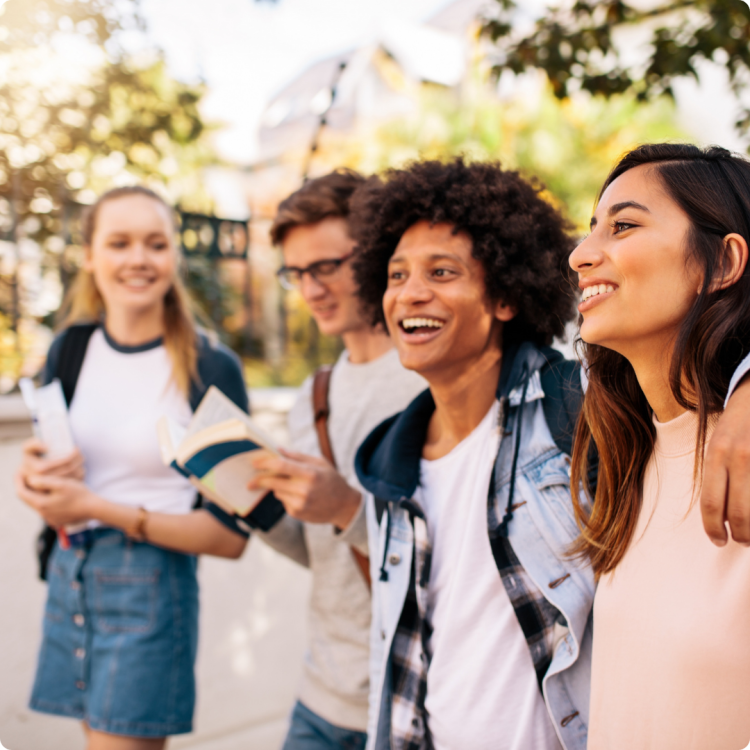 Four teens walking while holding books and smiling.