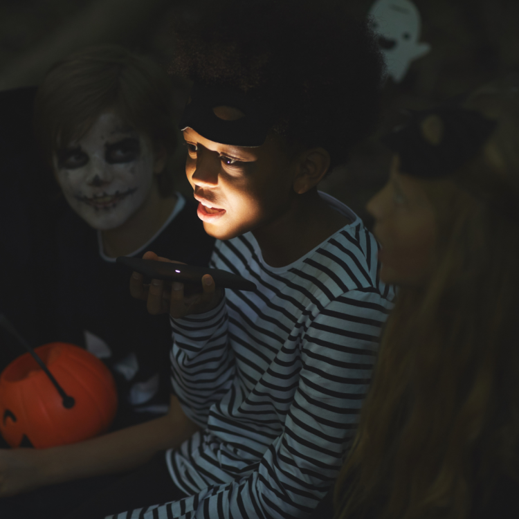 A child in a costume holding a light under their face to tell a scary story.